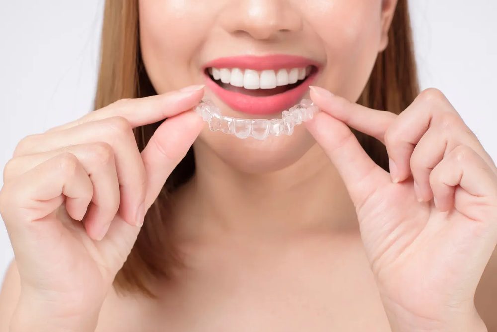 Smiling woman holding a clear aligner