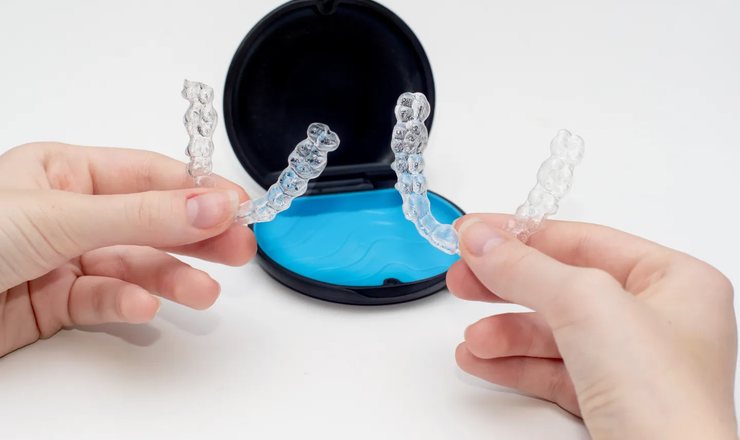 Hands lifting a pair of clear aligners out of their case