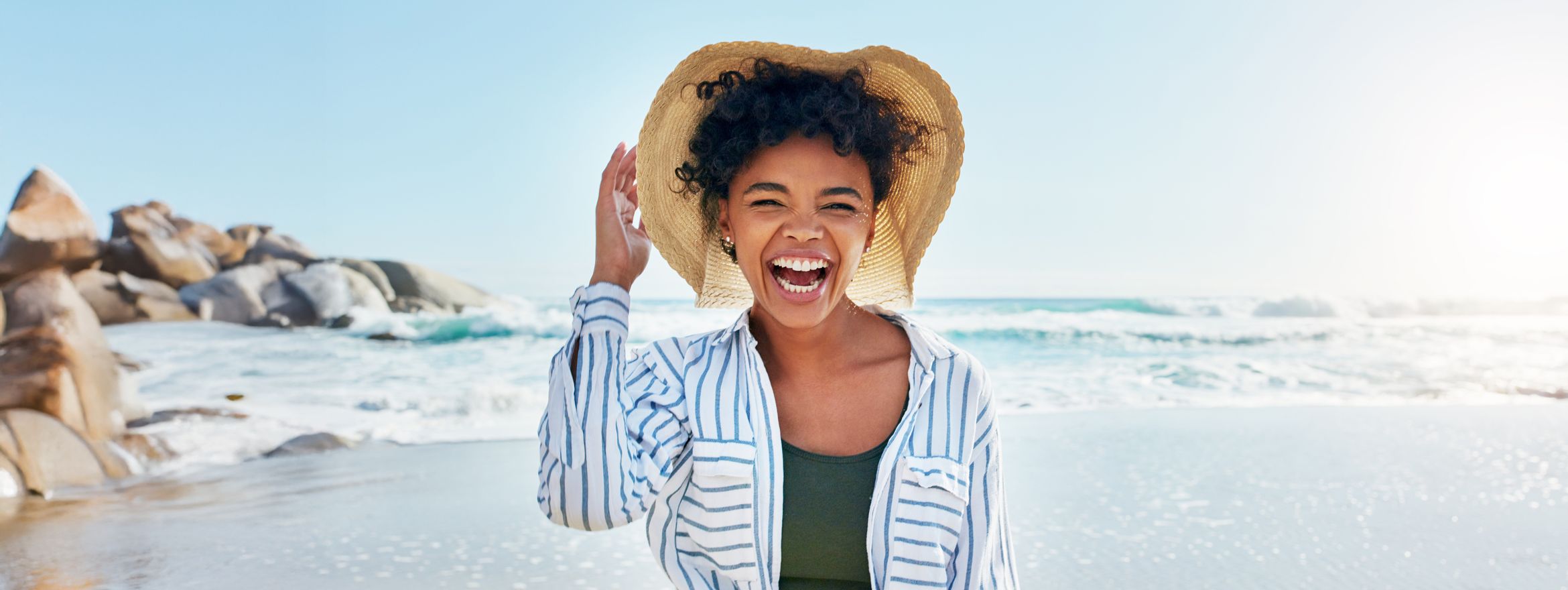 A woman in a straw hat laughing on a sunny beach