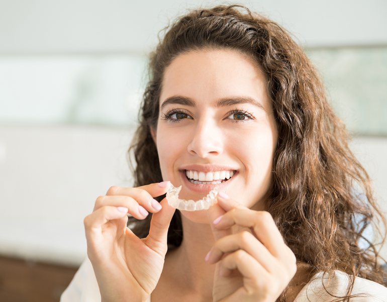 A woman holding up a clear aligner