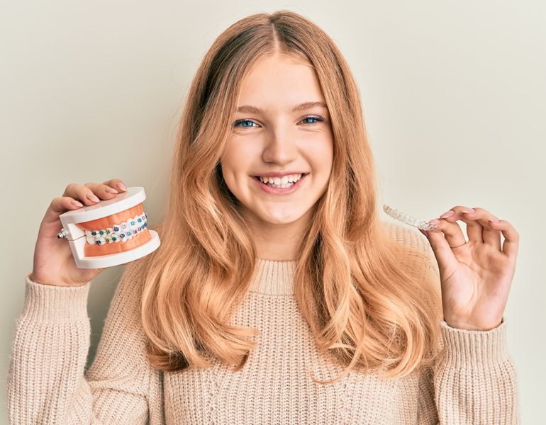 A girl holding a model of teeth with braces and a clear aligner