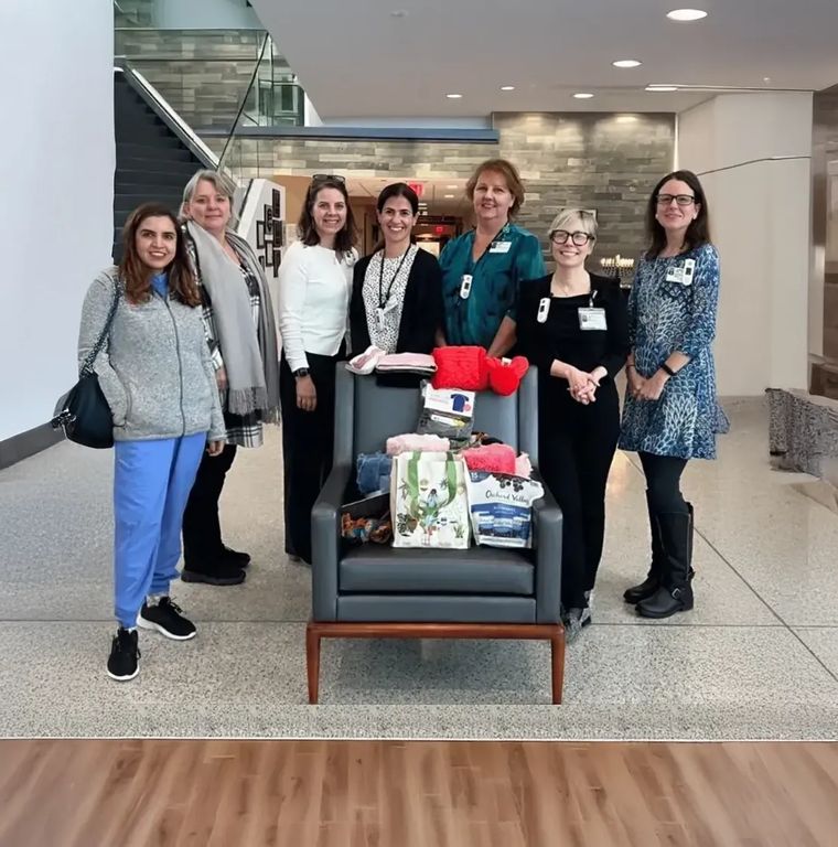Dr. Divya and six colleagues standing around an armchair piled with donations in a bright lobby