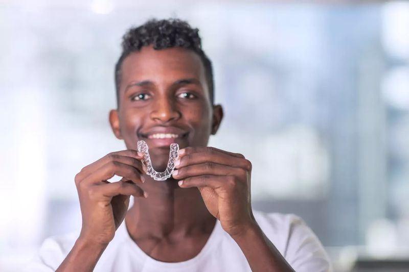 A smiling young man holding up a clear aligner