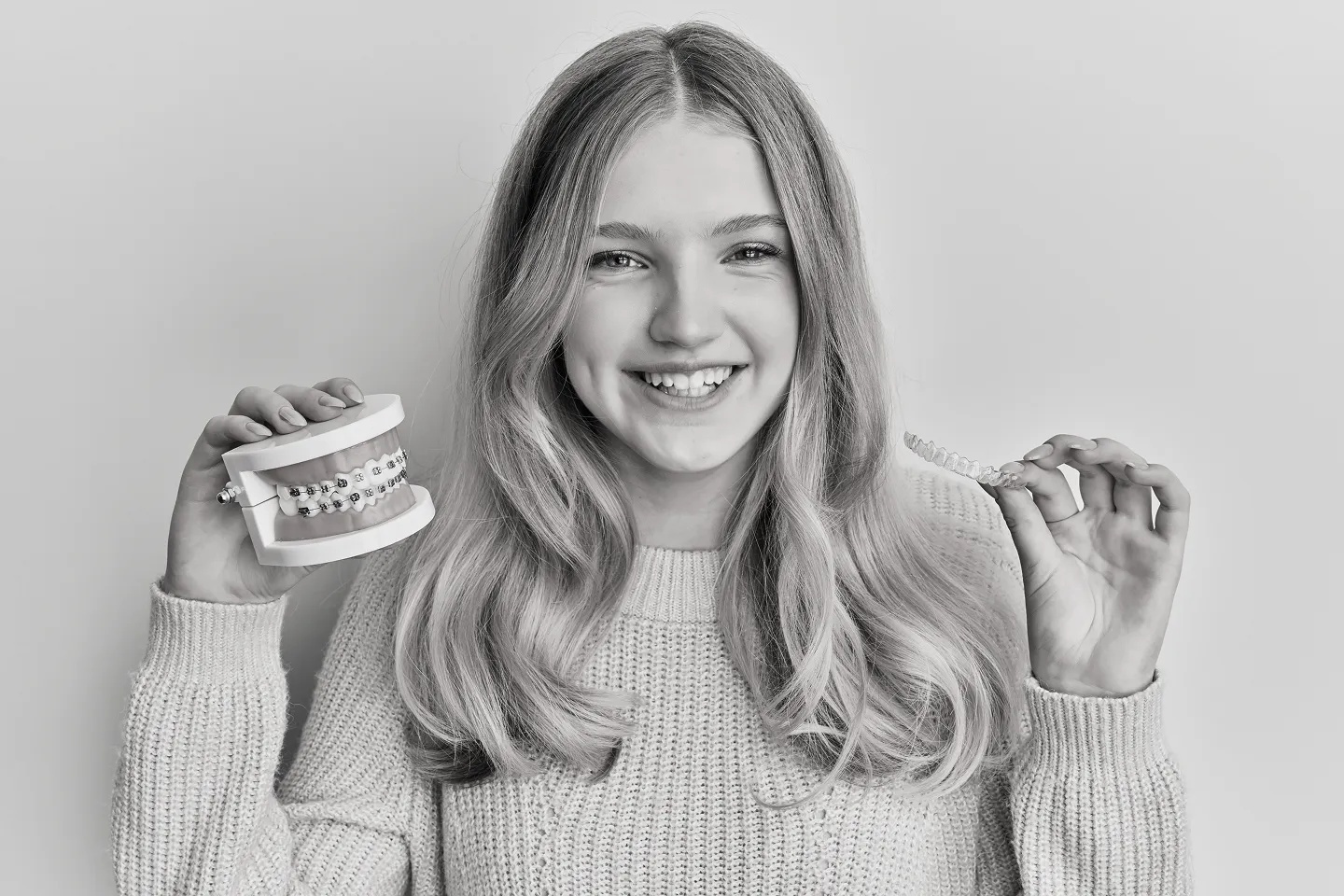 A smiling teenager holding a model of teeth with braces