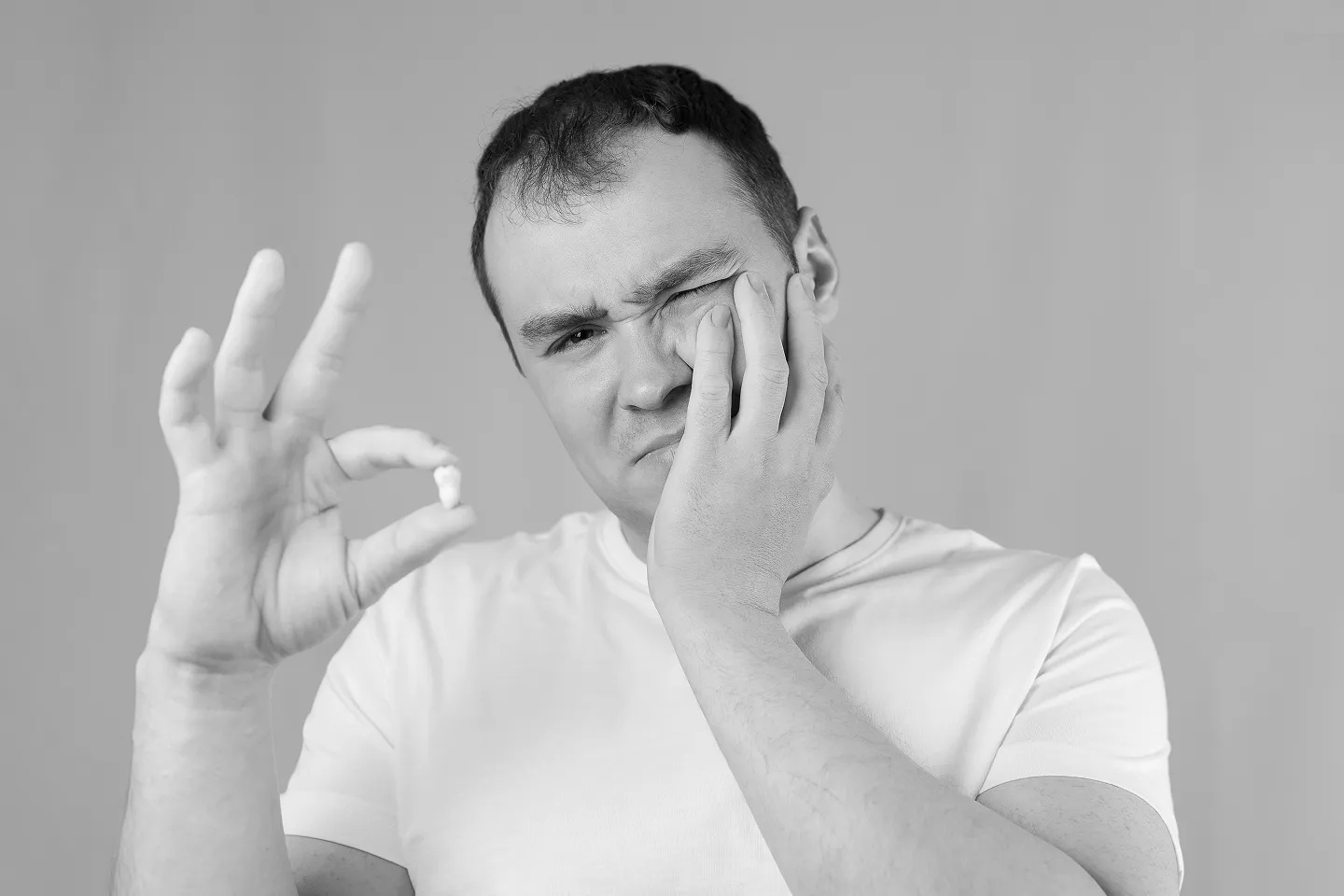 A man holding his jaw, pointing at an extracted wisdom tooth